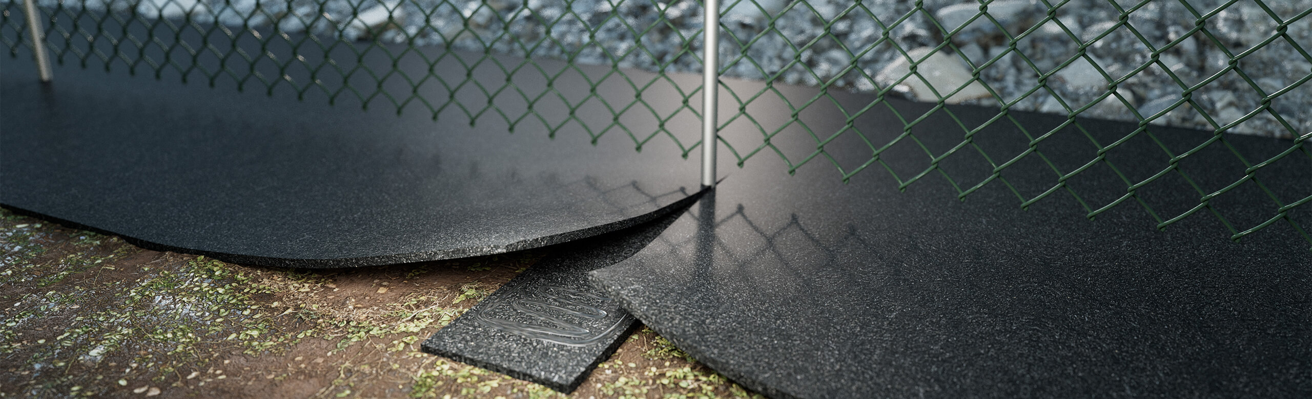 REGUPOL vegetation control 767 prevents plant growth under fences. UV-blocking, water-permeable, and environmentally friendly. REGUPOL vegetation control 767 growth-inhibiting mat under a chain-link fence for ecological and long-term vegetation prevention.